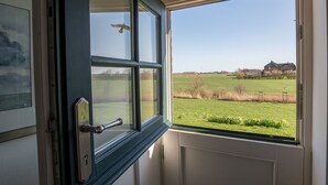 Una habitación con un ventanal grande, una puerta con picaporte y vistas a un campo verde y edificios.