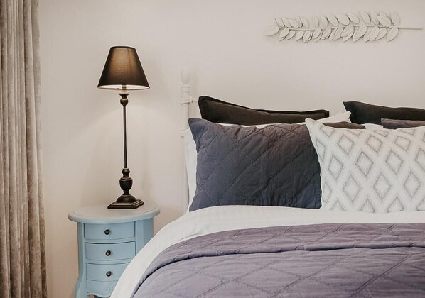 Een net opgemaakt bed met een gewatteerde deken, een bedlampje en een decoratief wandobject.