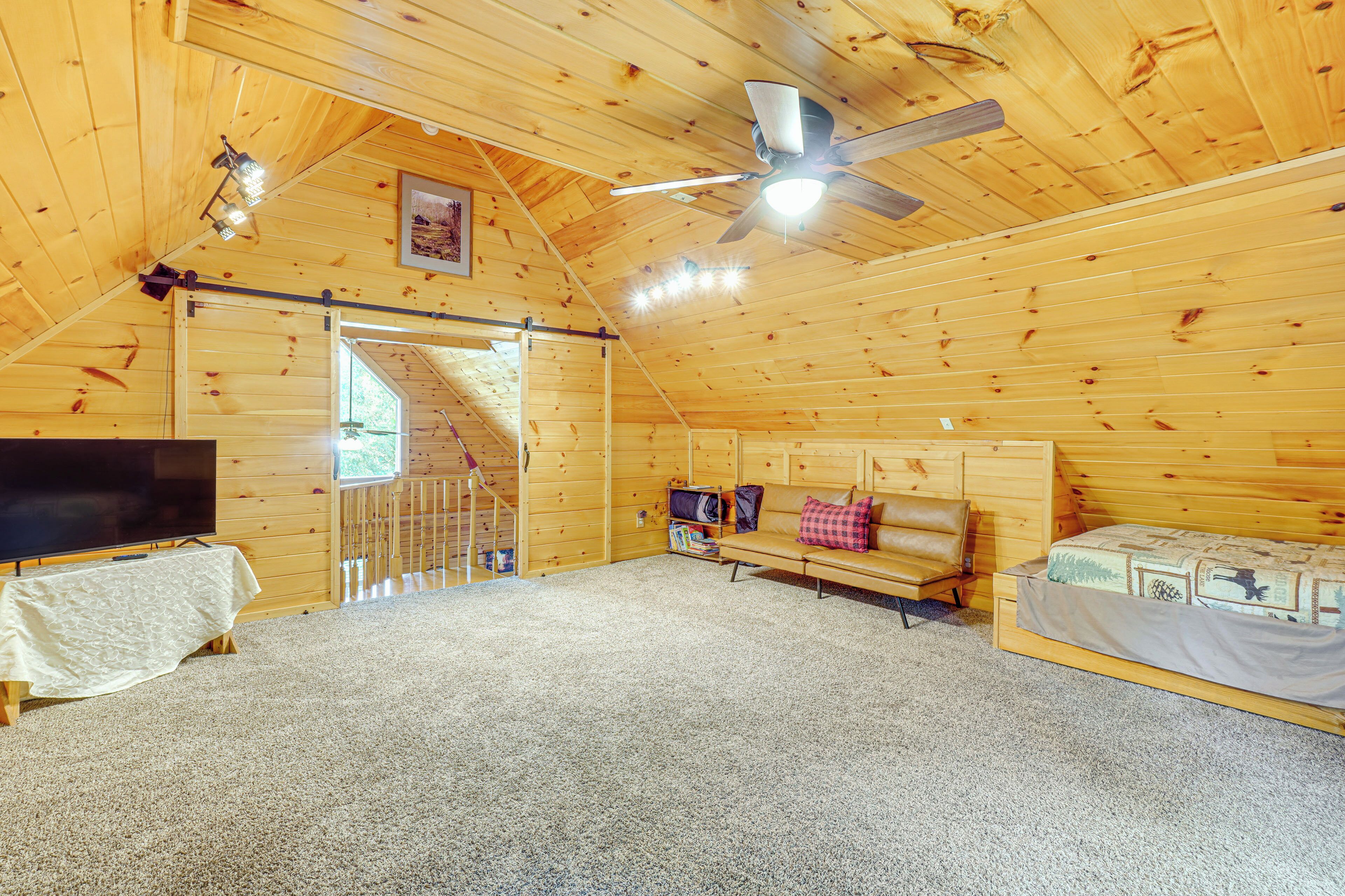Une cabane en bois chaleureuse, dotée d’un ventilateur de plafond, d’une télévision, d’un canapé et d’un lit.