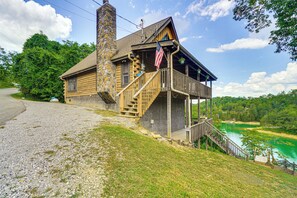 A log cabin with a stone chimney, wooden staircase, and a balcony with an American flag. - Douglas Lake Access: Family Cabin in Sevierville! (Sevierville)