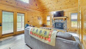 Interior de una cabaña de madera con chimenea, un sofá con una manta y un televisor.