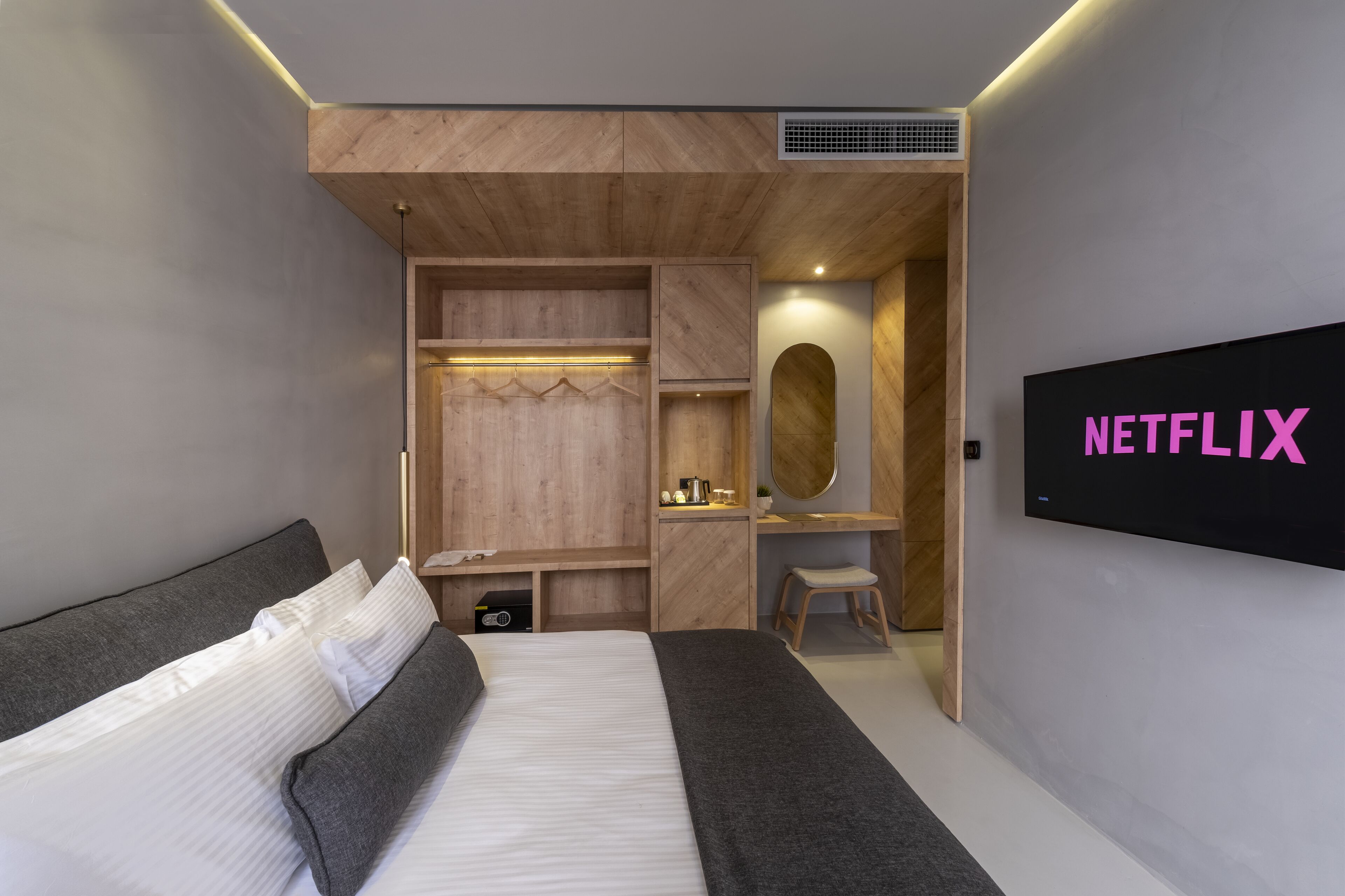 A modern bedroom with a bed, a TV mounted on the wall, and a wooden wardrobe.