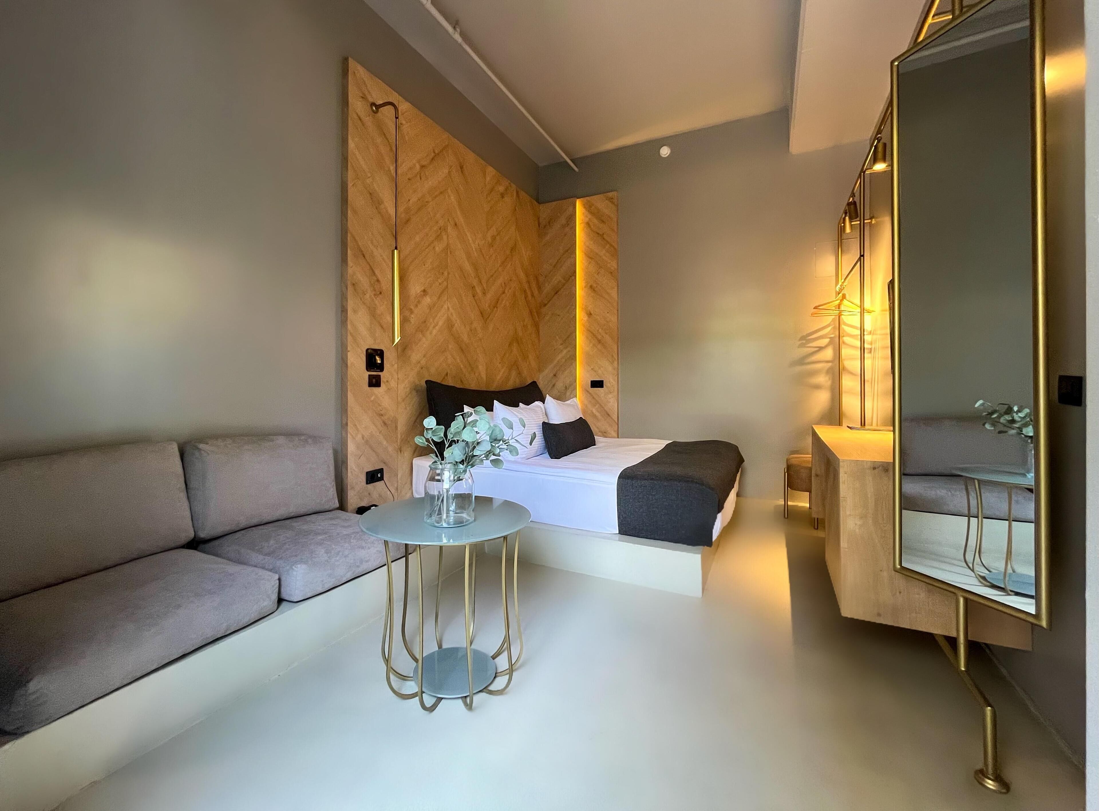 Een moderne slaapkamer met een bed, een bank, een klein rond tafeltje en een grote spiegel.