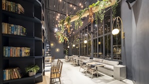 Una biblioteca moderna con estanterías, zonas de descanso y plantas colgantes.