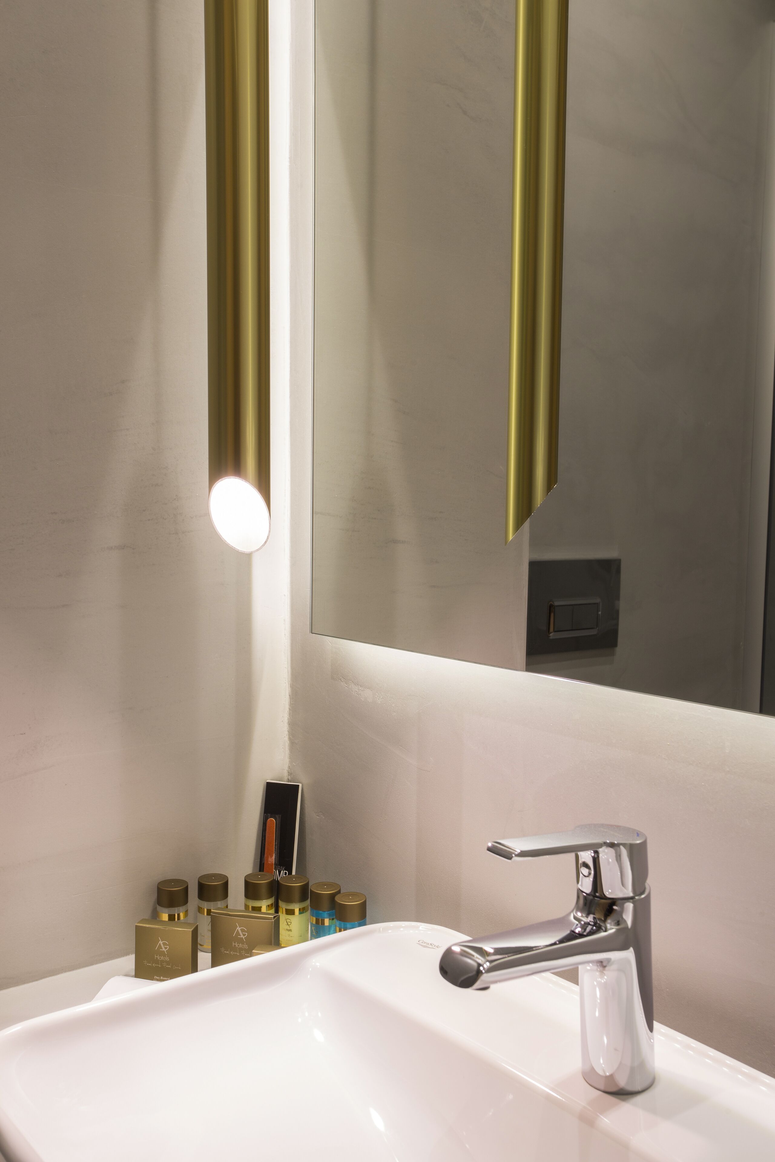 A modern bathroom with a white sink, chrome faucet, and gold-colored toiletries.