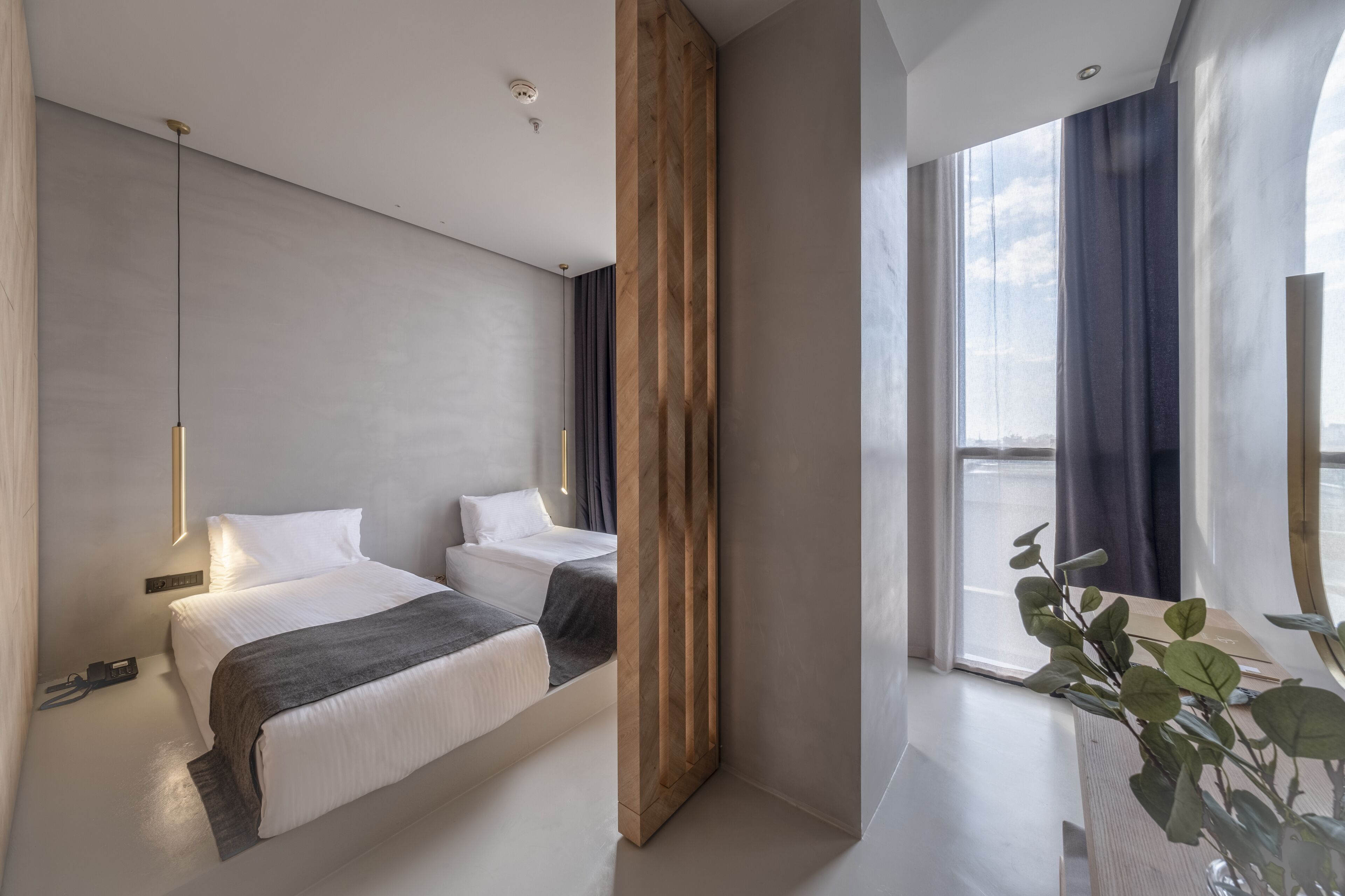 A modern hotel room with a large bed, a wooden accent wall, and a view of the city through large windows.