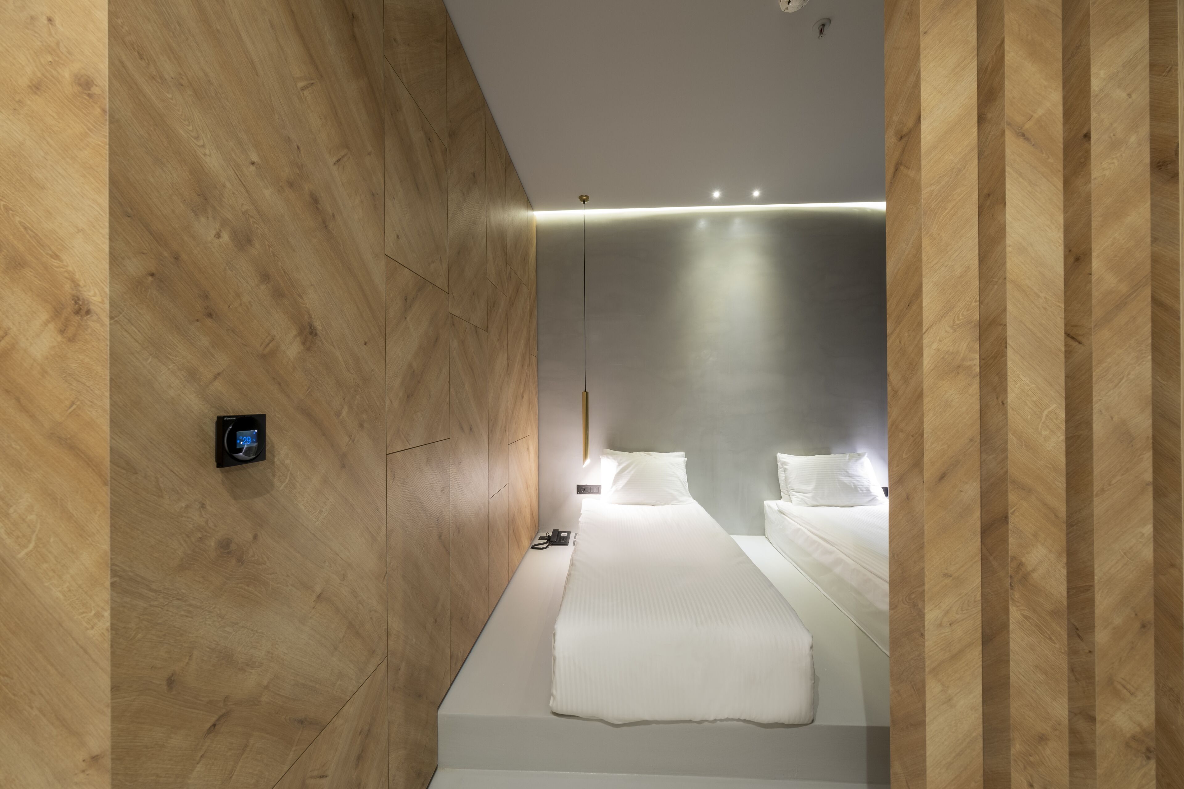 A modern hotel room with wooden panel walls, a large bed with white linens, and a bedside table.