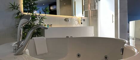 A modern bathroom with a large bathtub, a mirror, and a potted plant.