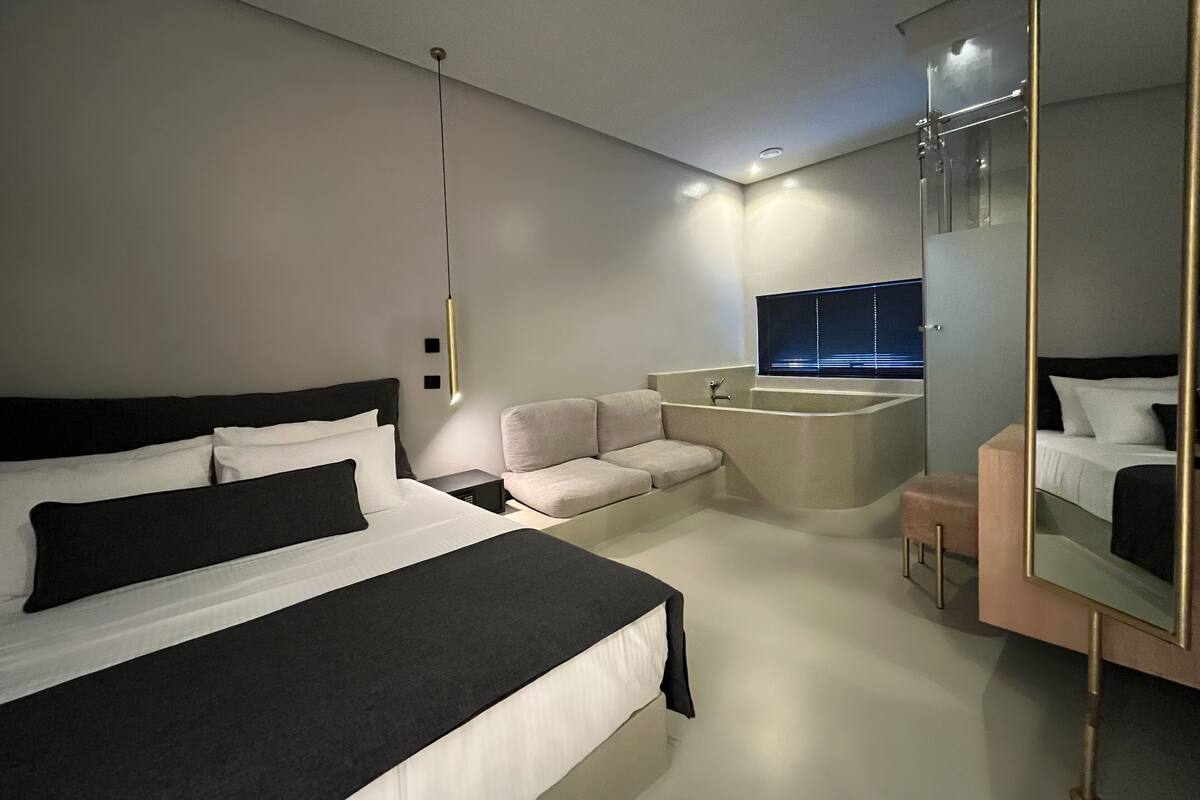 Ein modernes Hotelzimmer mit einem großen Bett, einer Sitzecke, einer Badewanne und einem großen Spiegel.