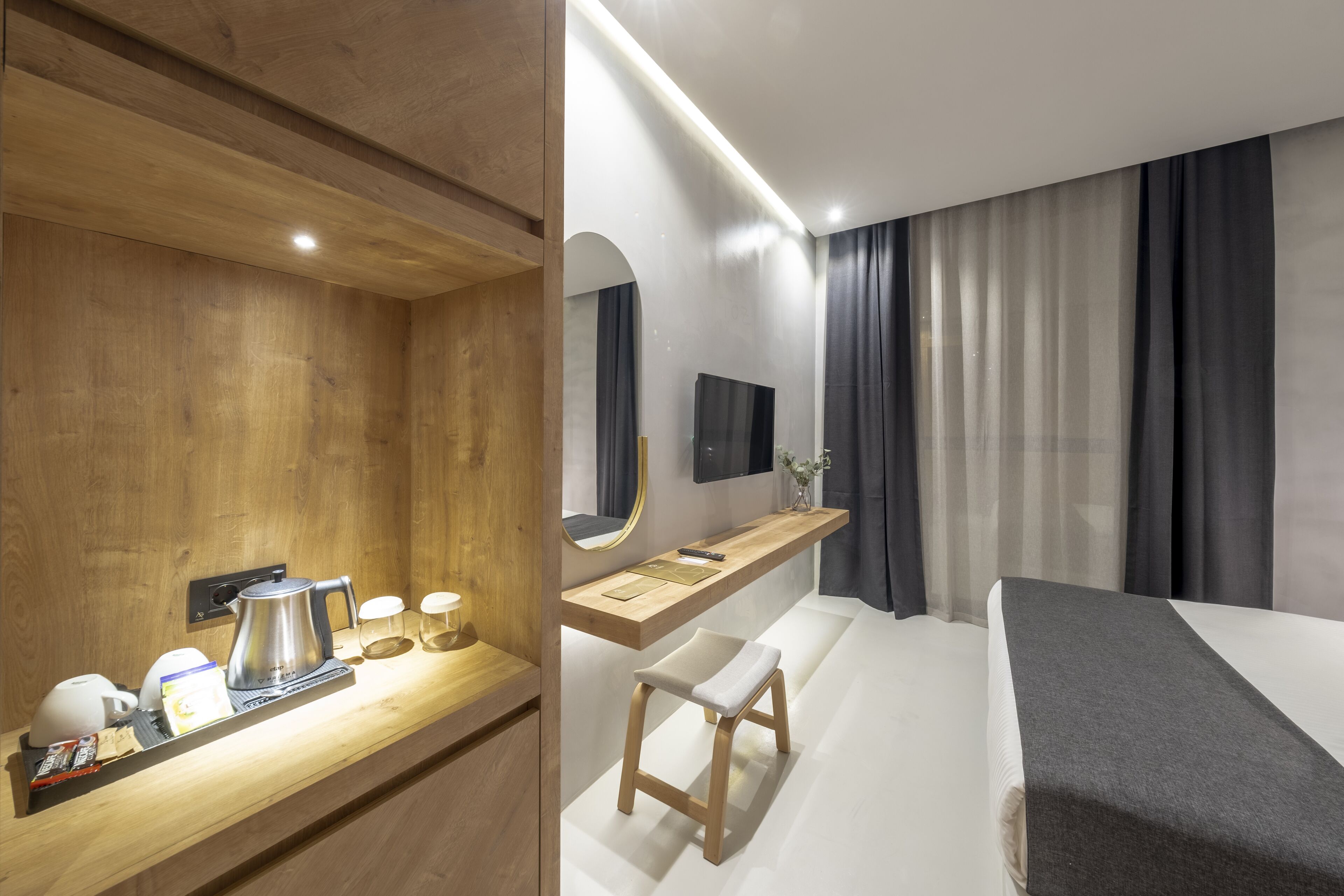 Une chambre d’hôtel moderne équipée d’un bureau en bois, d’un lit, d’une télévision et d’un espace salle de bain.
