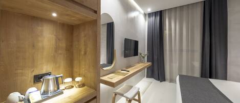 Ein modernes Hotelzimmer mit Schreibtisch aus Holz, einem Bett, einem Fernseher und einem Badebereich.
