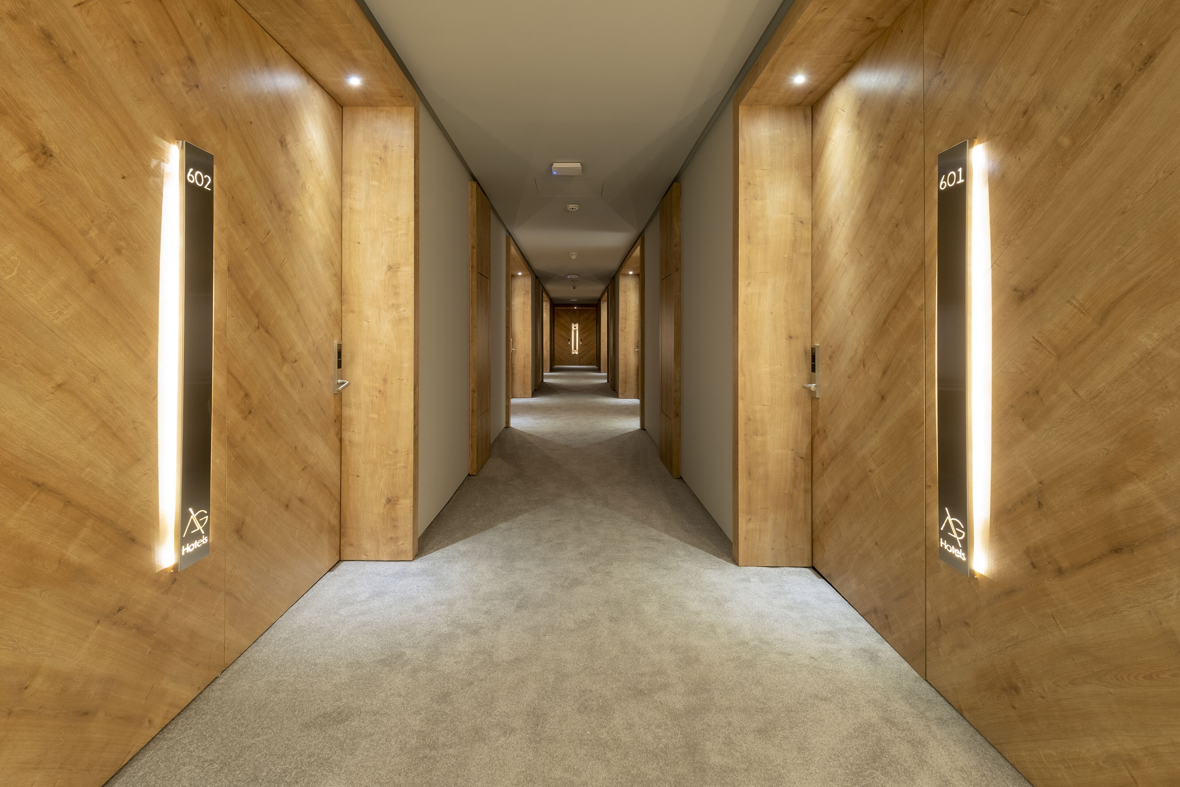 A modern hotel hallway with wooden walls and carpeted floors.