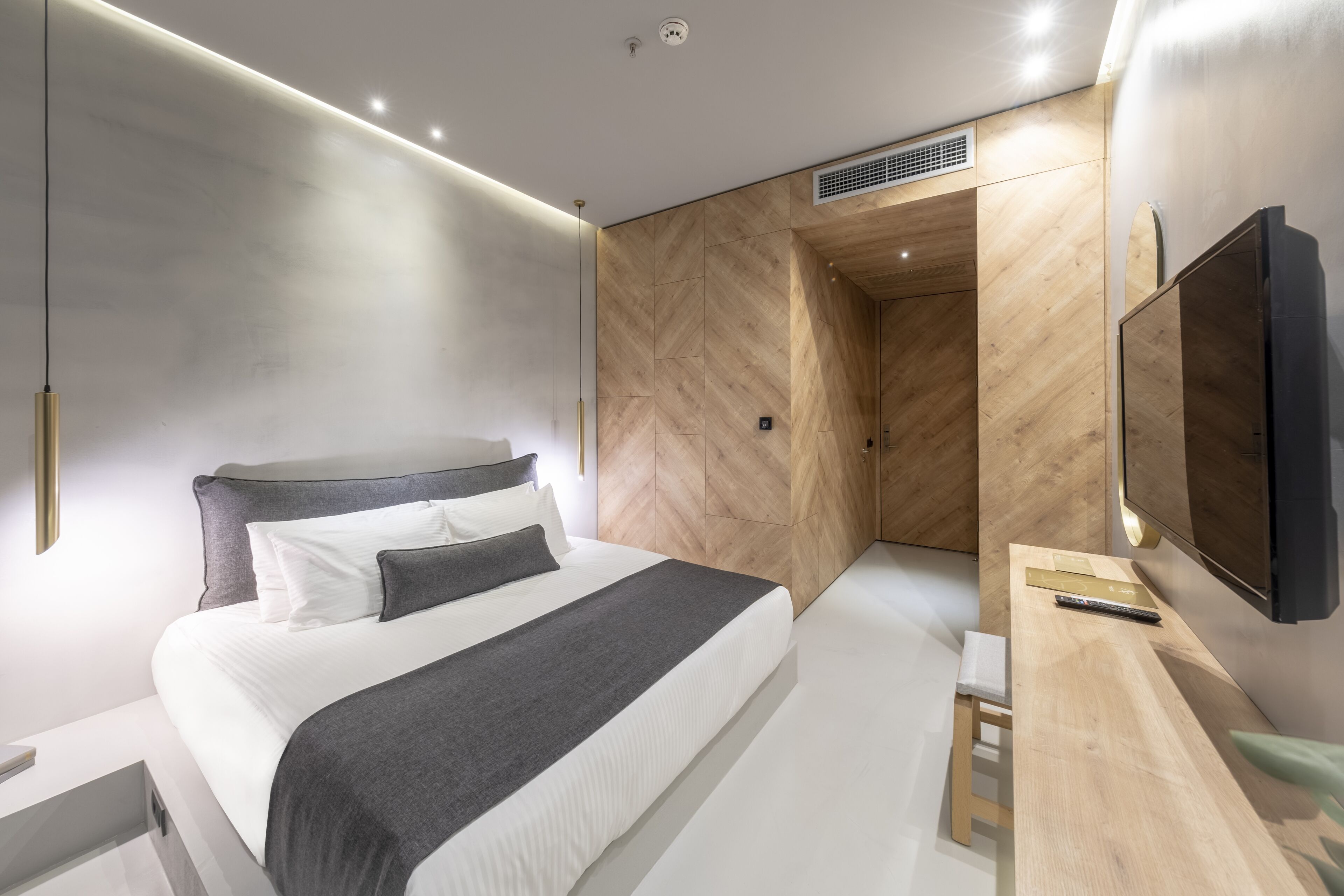 Ein modernes Hotelzimmer mit einem großen Bett, einer Wandvertäfelung aus Holz, einem Schreibtisch mit Flachbildfernseher und einem eingebauten Kleiderschrank.