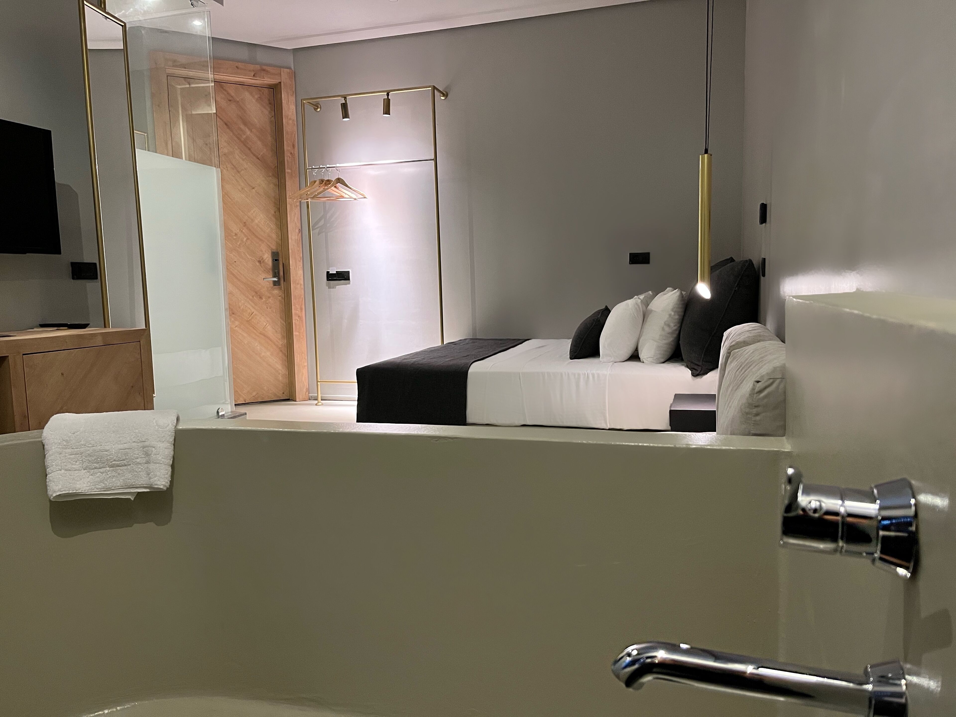 A modern bedroom with a bed, a wooden wardrobe, a mirror, and a bathroom with a bathtub.