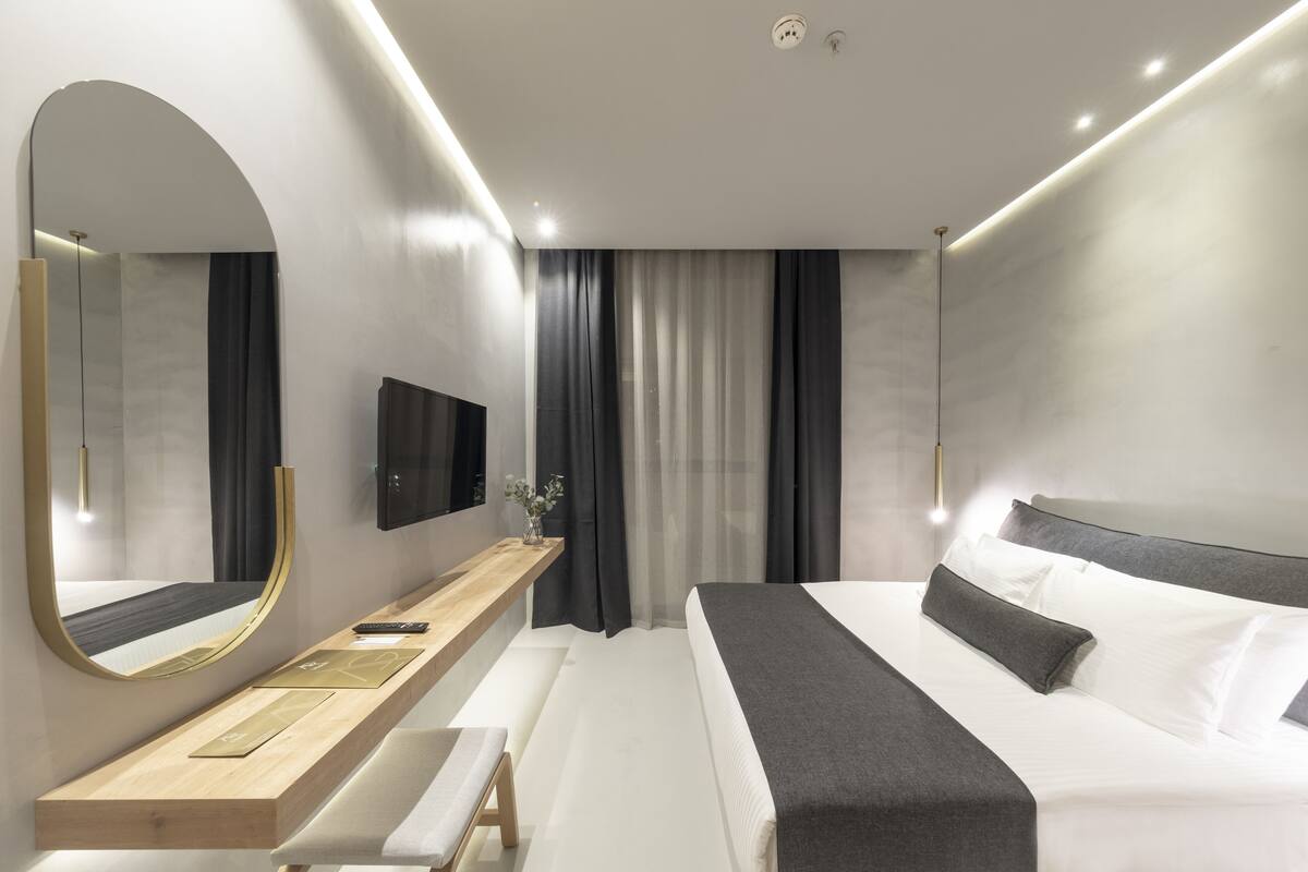 Ein modernes Hotelzimmer mit einem großen Bett, einem Nachttisch, einem Spiegel und einem Fernseher.