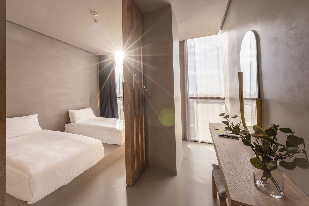 Ein modernes Hotelzimmer mit zwei Betten, einem Holztisch und einem großen Fenster.