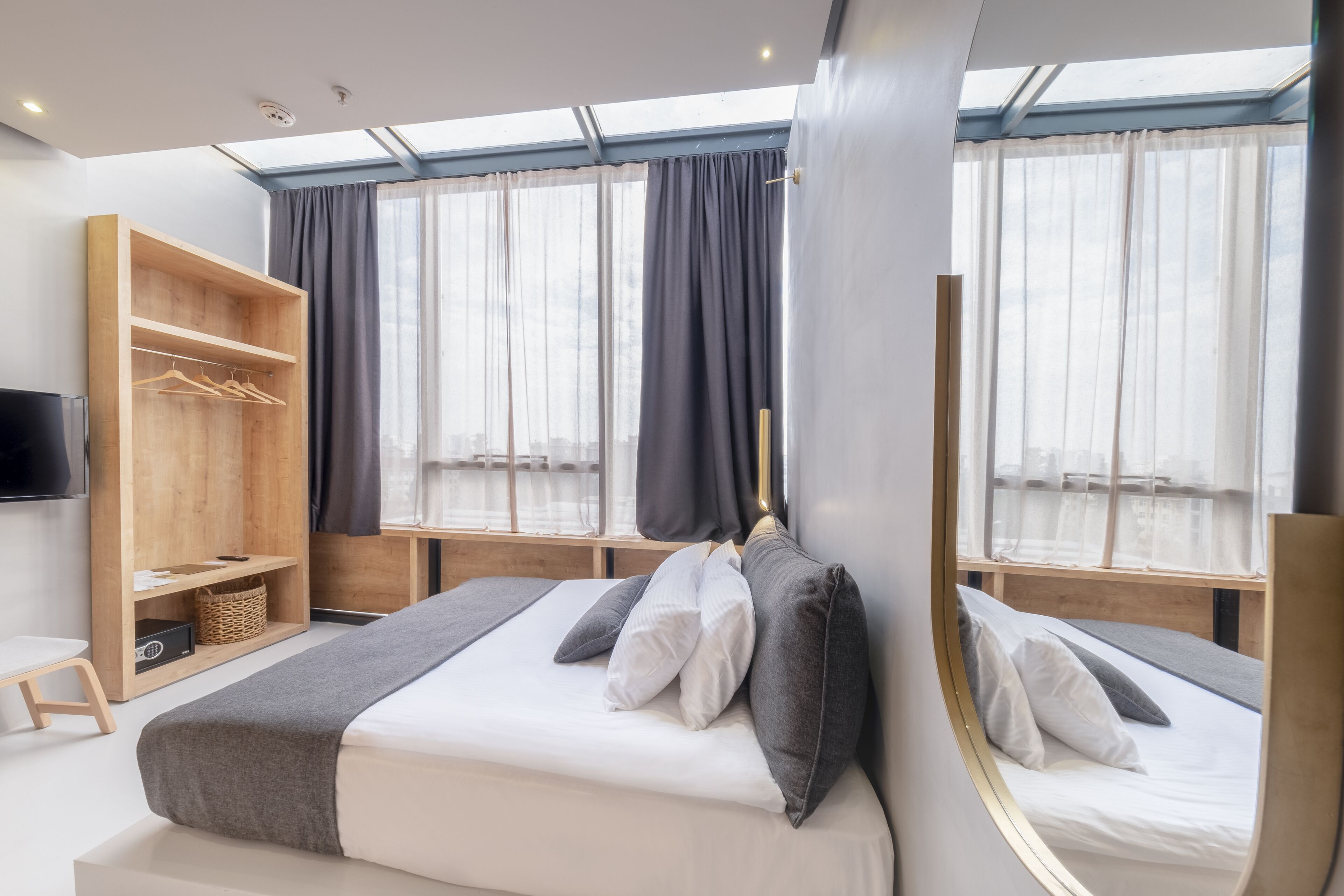 Una habitación de hotel moderna con una cama grande, un armario de madera, una mesita pequeña y un televisor.