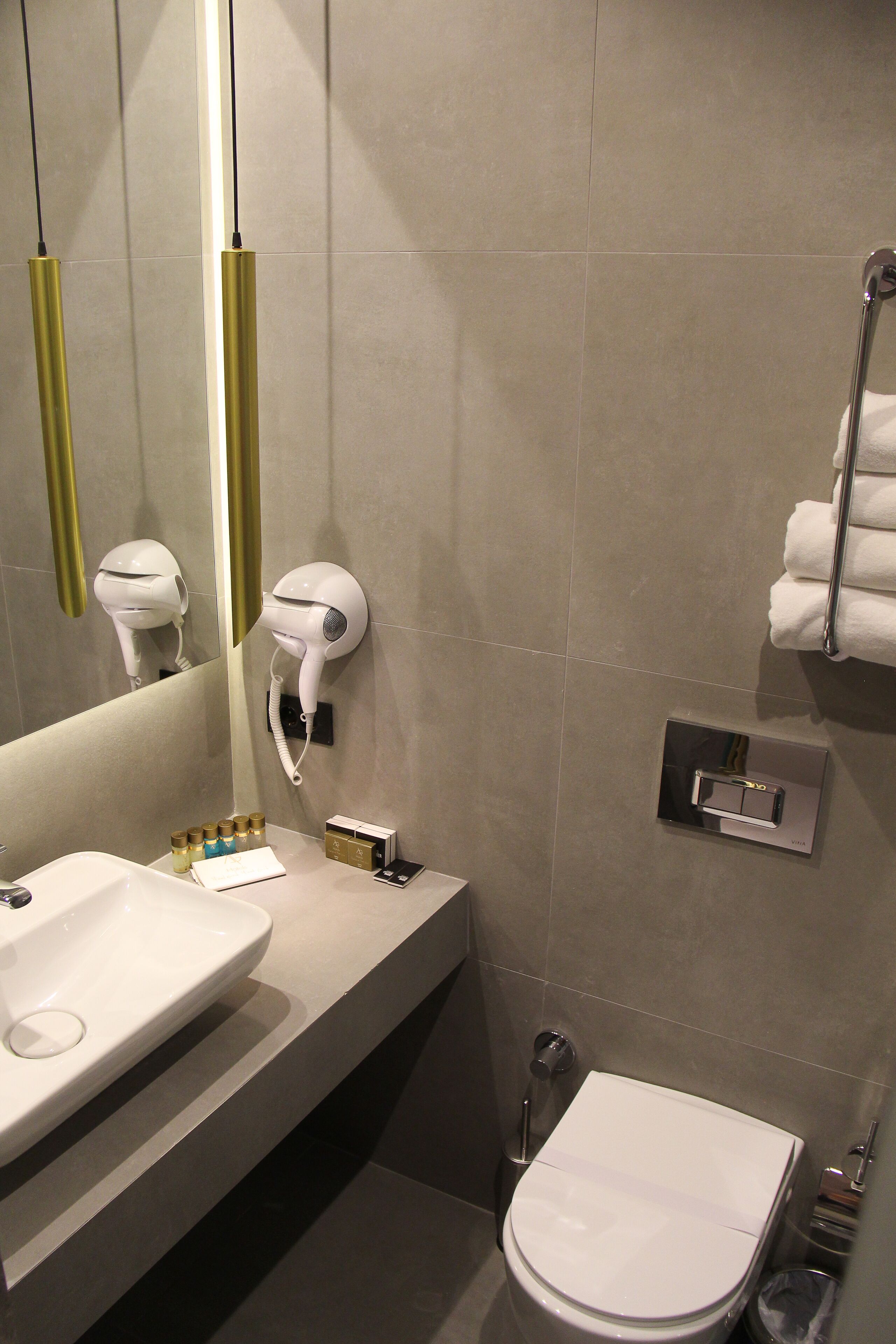 A modern bathroom with a sink, mirror, hairdryer, towel rack, and toilet.