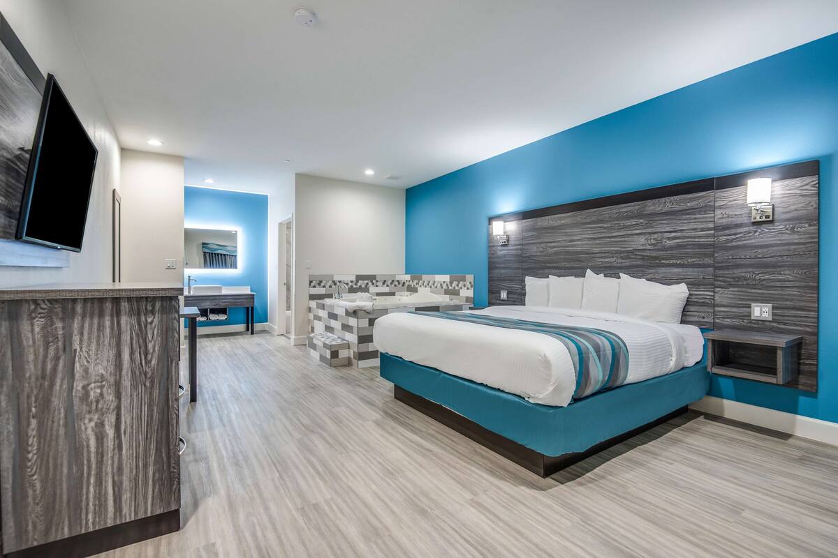 A modern hotel room with a large bed, a vanity with a mirror, and a small seating area.