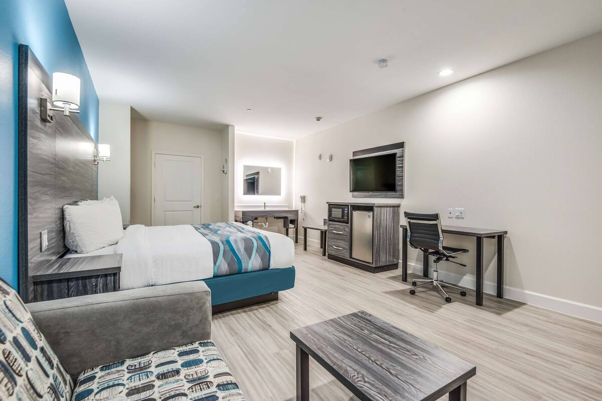 A modern hotel room with a bed, a sofa, a desk, and a TV.