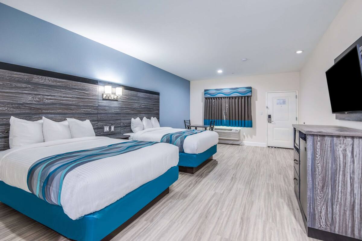 A hotel room with two beds, a desk, and a TV.