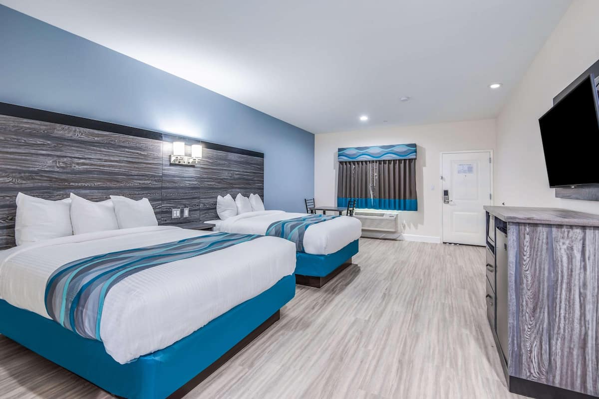A hotel room with two beds, a desk, a TV, and a door.