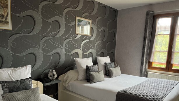 Une chambre d’hôtel avec deux lits, une tête de lit à motifs, un tableau encadré et une fenêtre avec des rideaux.