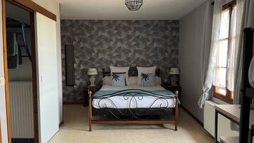Een slaapkamer met een wand met een geometrisch patroon, een bed met houten frame, twee nachtkastjes met lampen, een hangende lamp en een raam met gordijnen.