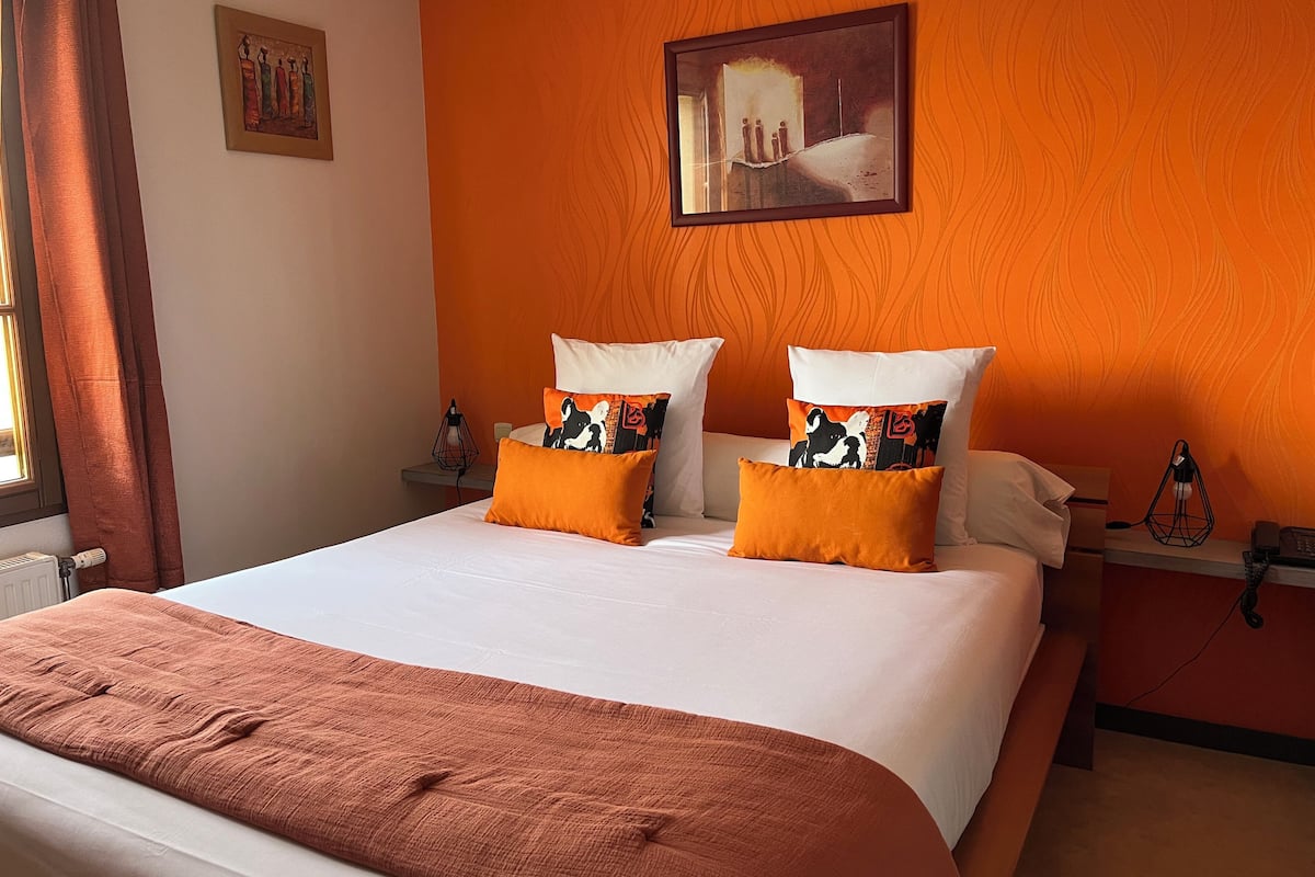 Une chambre d’hôtel avec un grand lit, des murs orange et un tableau au-dessus du lit.