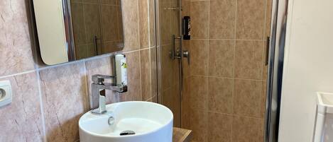 Un baño con lavamanos blanco, espejo y zona de ducha.