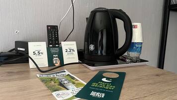 Una habitación de hotel con cafetera, control remoto, botella de agua y un folleto sobre la mesa.