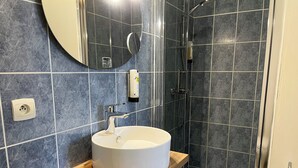 Une salle de bain avec un lavabo blanc, un miroir, une douche et un sol carrelé.