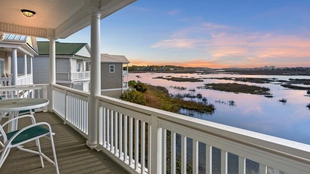 A covered porch with a view of a water body and distant buildings. - Stunning marsh view home, gorgeously furnished, private pool - walk to beach - perfect area (North Myrtle Beach)