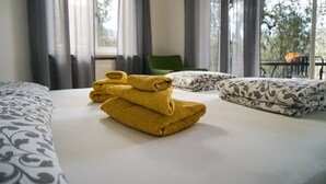 Una camera d'albergo con un letto, una poltrona verde e vista sugli alberi dalla finestra.