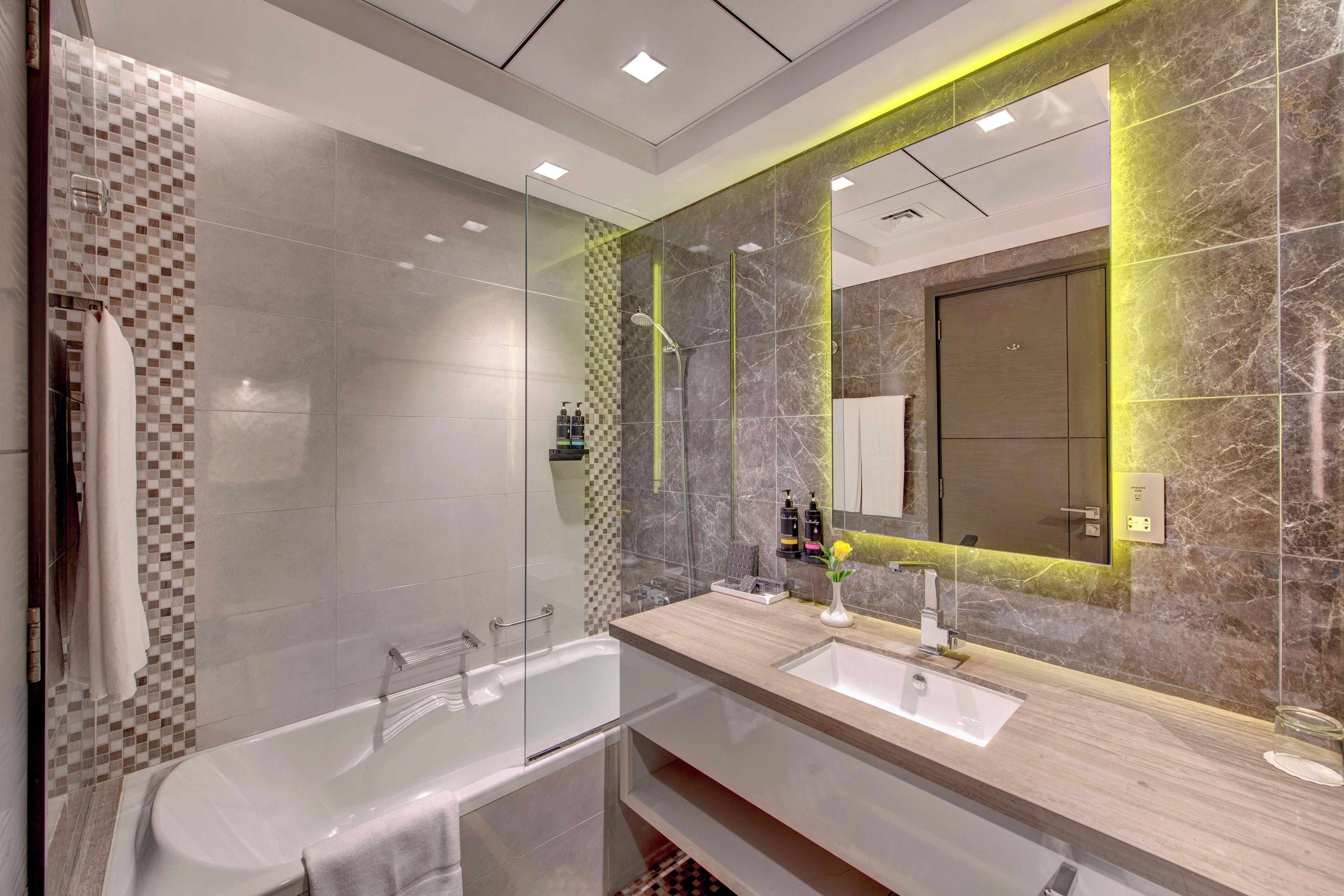A modern bathroom with a glass-enclosed shower, a double sink vanity, and a large mirror with a marble backsplash.
