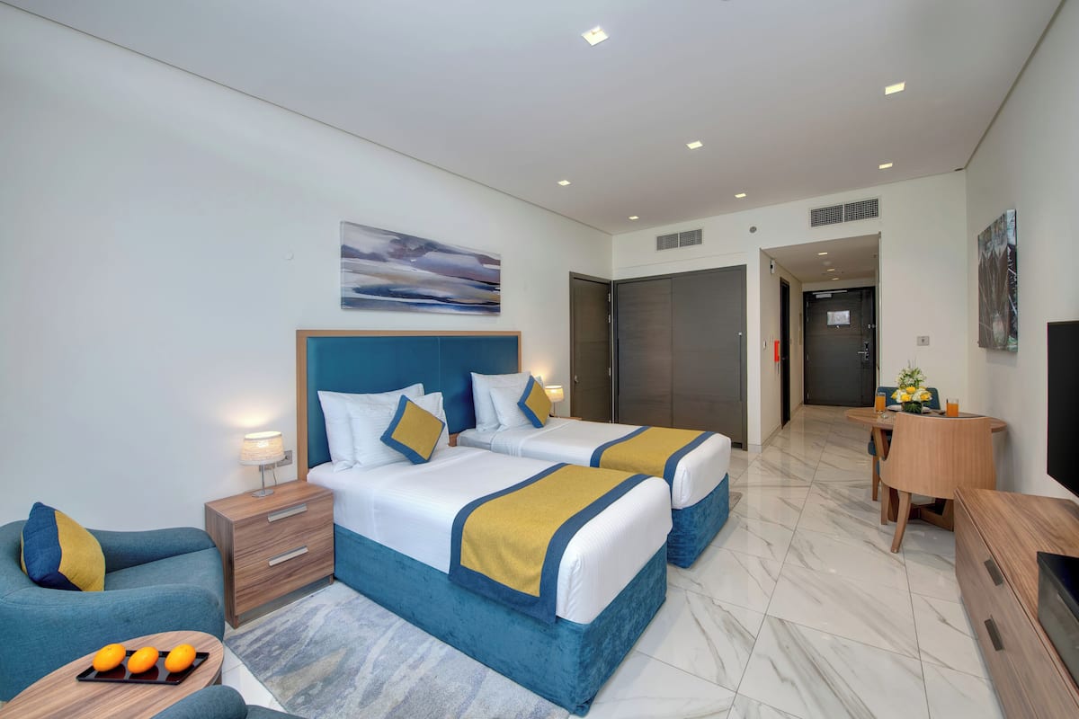 Une chambre d’hôtel moderne avec deux lits, un canapé, une petite table avec des oranges et un téléviseur.