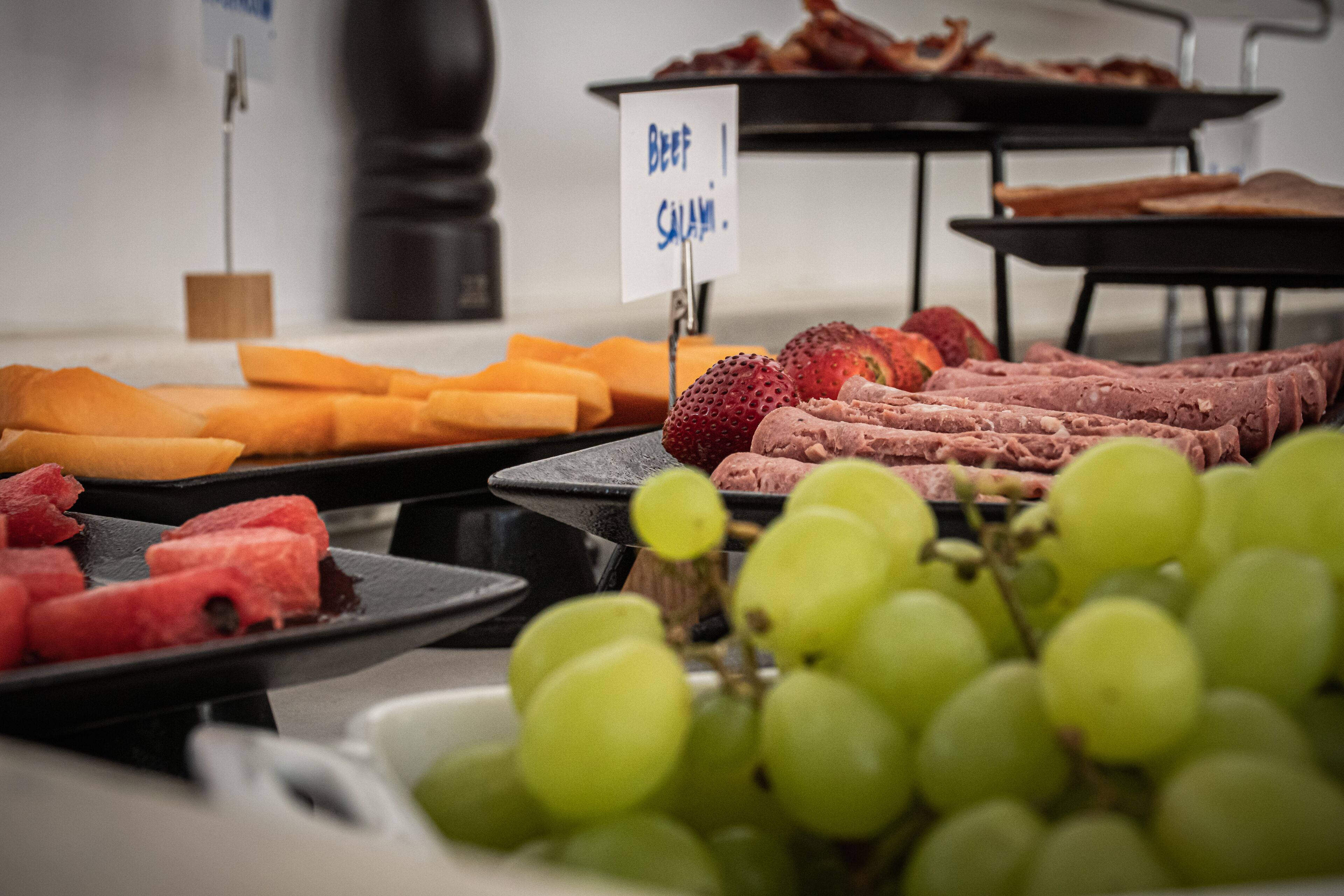 A buffet with various food items including watermelon, grapes, and sliced meats.