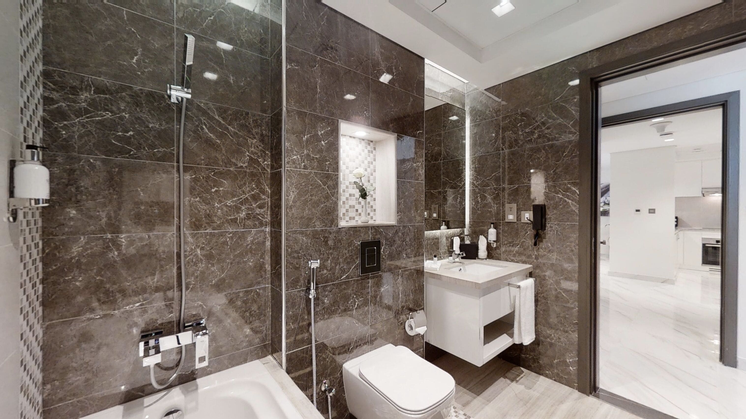 A modern bathroom with a marble floor, a bathtub, a toilet, and a sink with a mirror above it.
