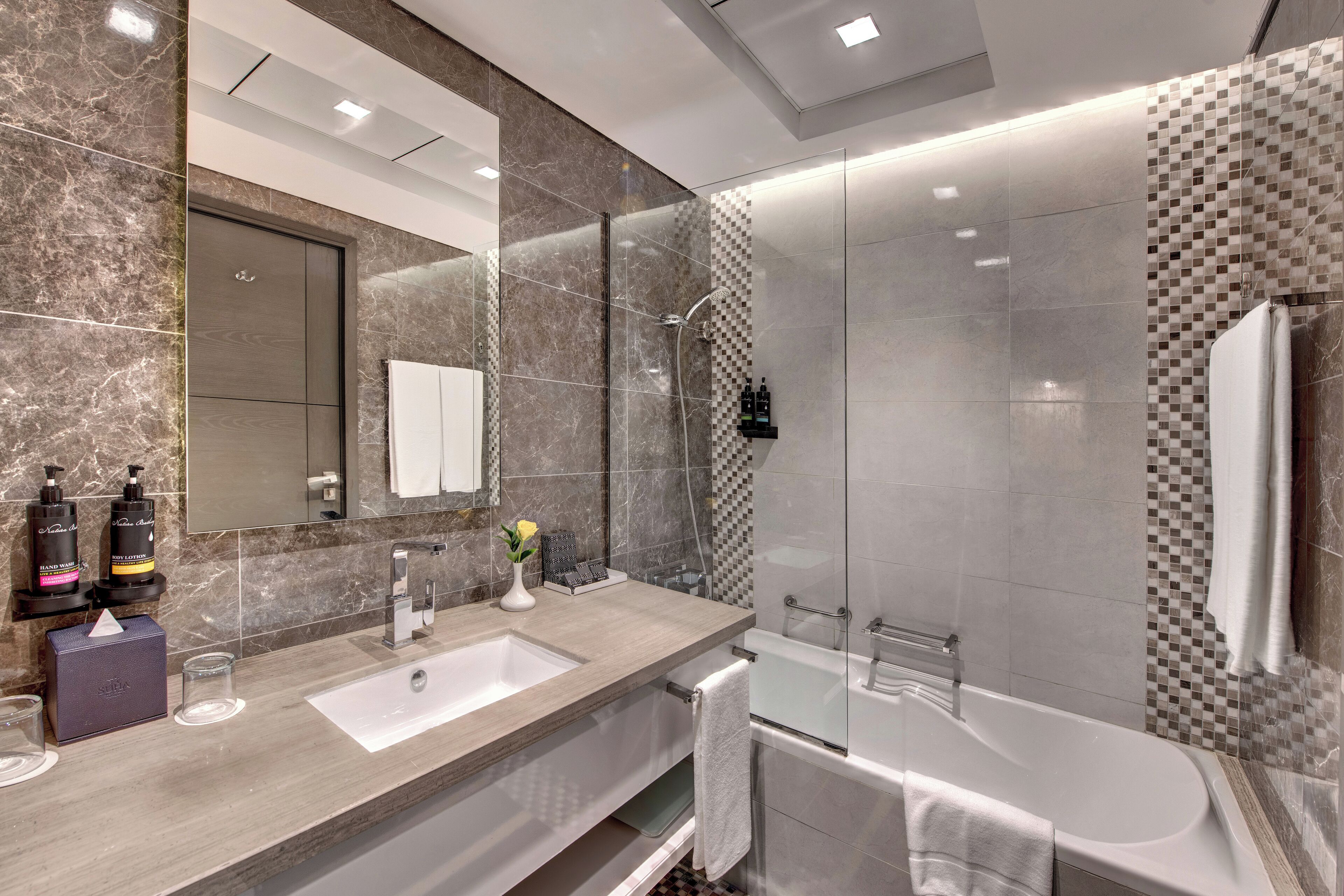 Une salle de bain moderne avec un meuble-lavabo en marbre, un grand miroir, une douche à parois de verre et une baignoire.