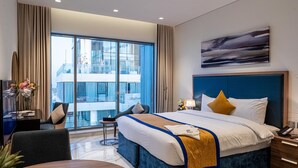 Een moderne hotelkamer met een groot bed, een bureau met een computer, een stoel en uitzicht op een gebouw door grote ramen.
