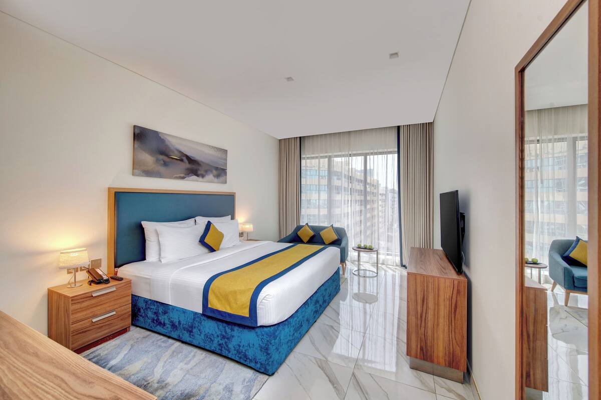 Une chambre d’hôtel moderne avec un grand lit, des tables de chevet, une télévision et une vue sur la ville.
