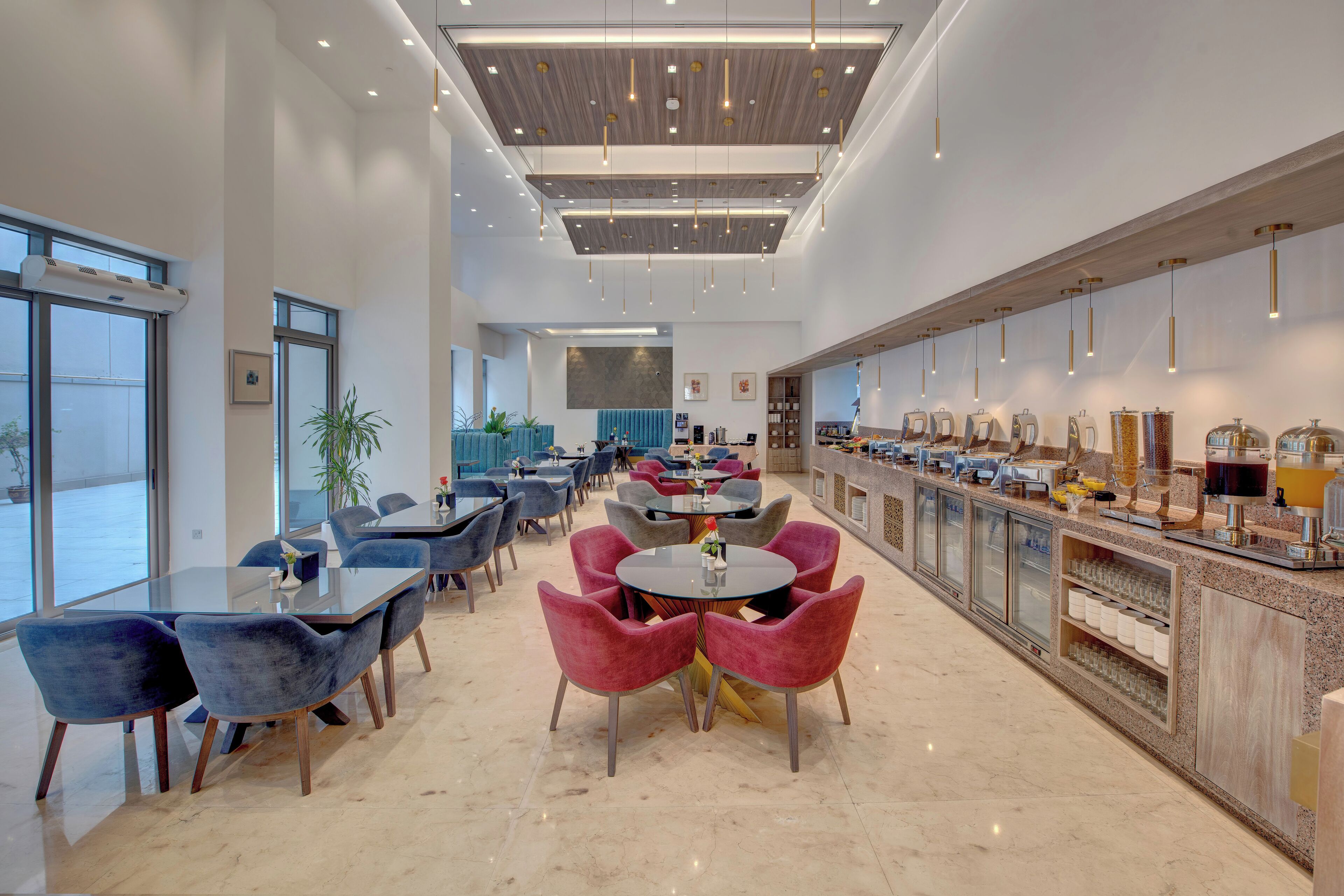 Un hall d’hôtel moderne doté d’un espace salon central, d’un bar offrant divers services et de grandes fenêtres laissant entrer la lumière naturelle.