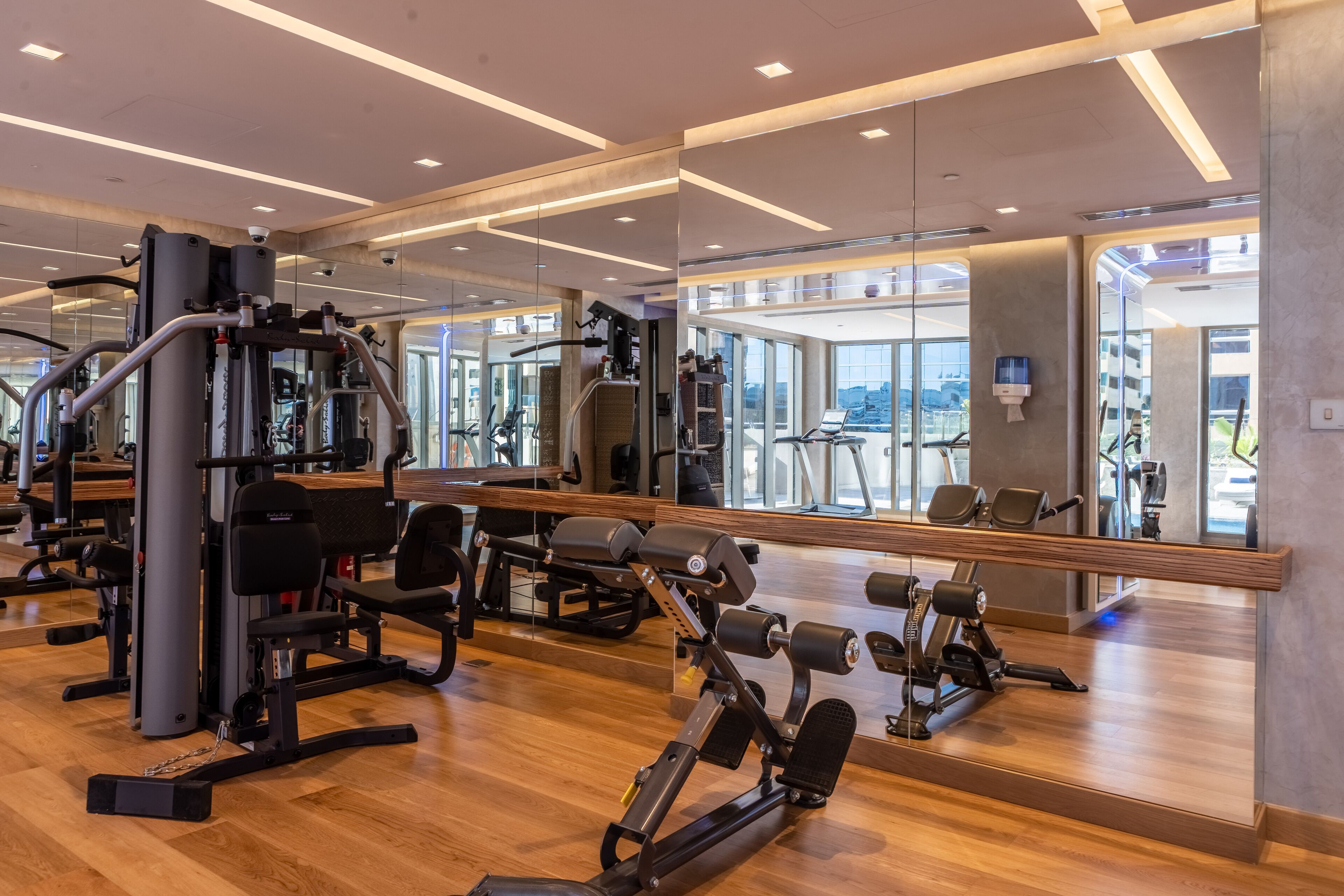 A modern gym with various exercise machines, large mirrors, and a wooden floor.