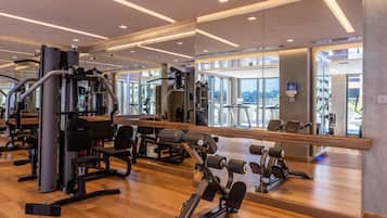 A modern gym with various exercise machines, large mirrors, and a wooden floor.