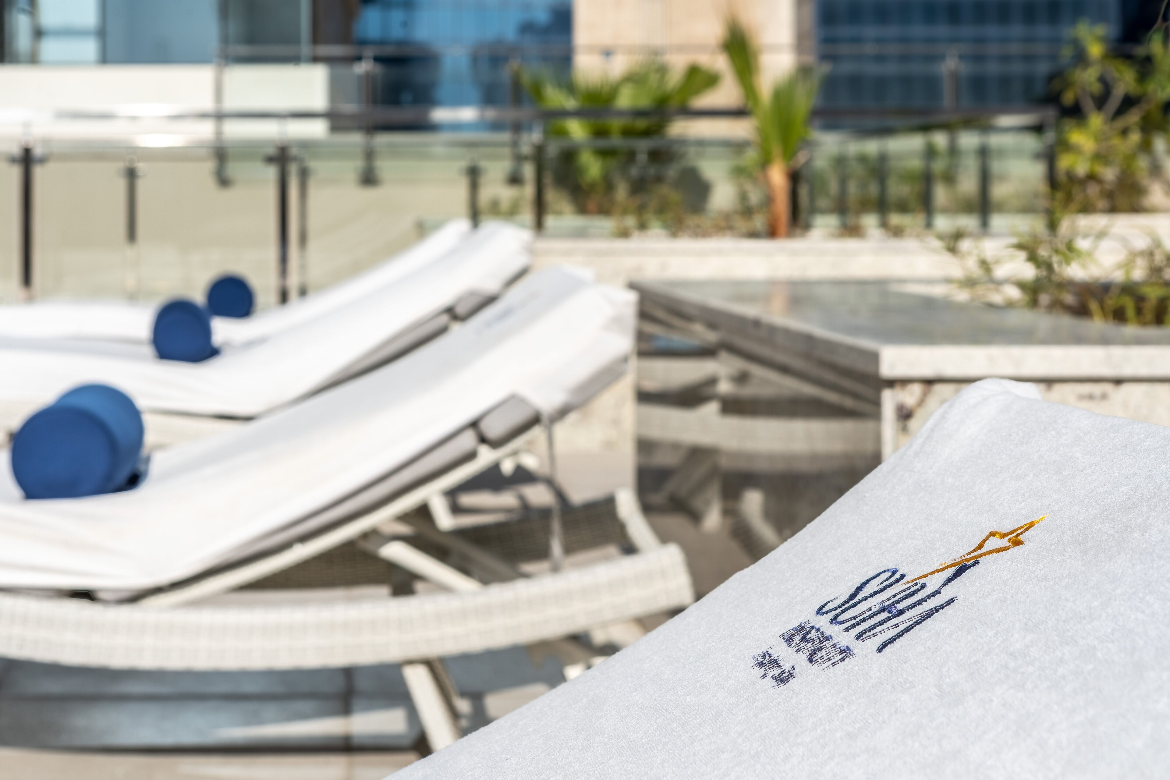 Un espace aménagé au bord de la piscine, avec des chaises longues et une serviette ornée d’un logo.