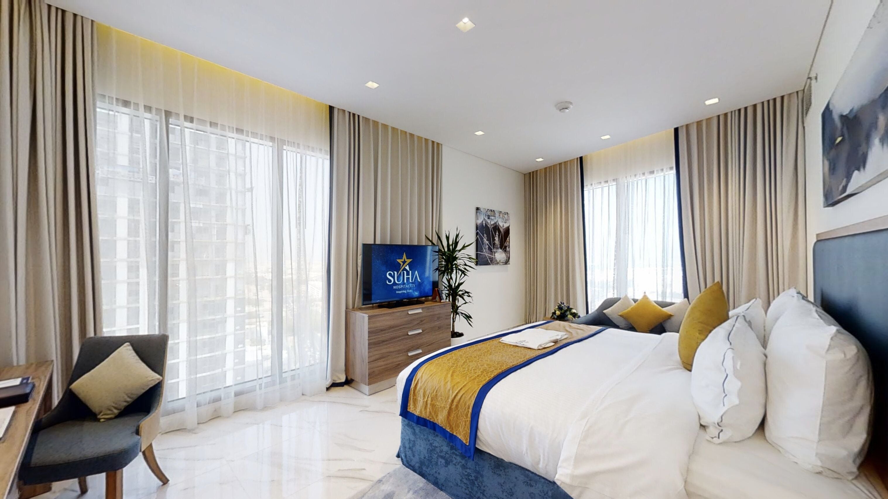 A modern hotel room with a large bed, a TV, a desk, and a plant.
