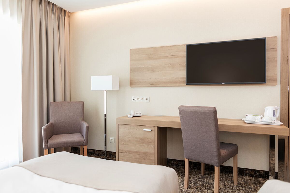 Habitación de hotel con cama, escritorio, dos sillas, televisión de pantalla plana, lámpara y cafetera.