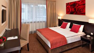 Een hotelkamer met een bed, een bureau, een stoel, een nachtkastje en een schilderij van rode rozen.