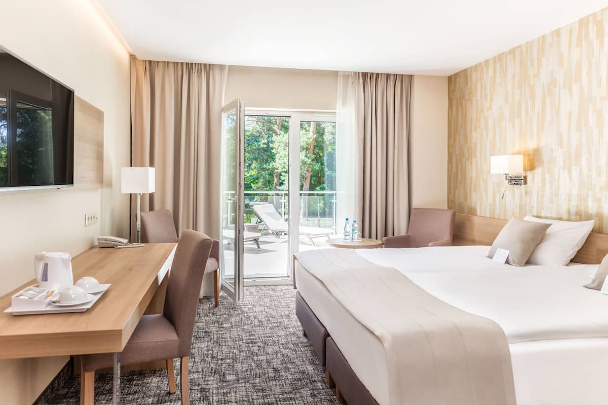 A hotel room with a bed, a desk, a chair, a lamp, and a view of the outdoors.