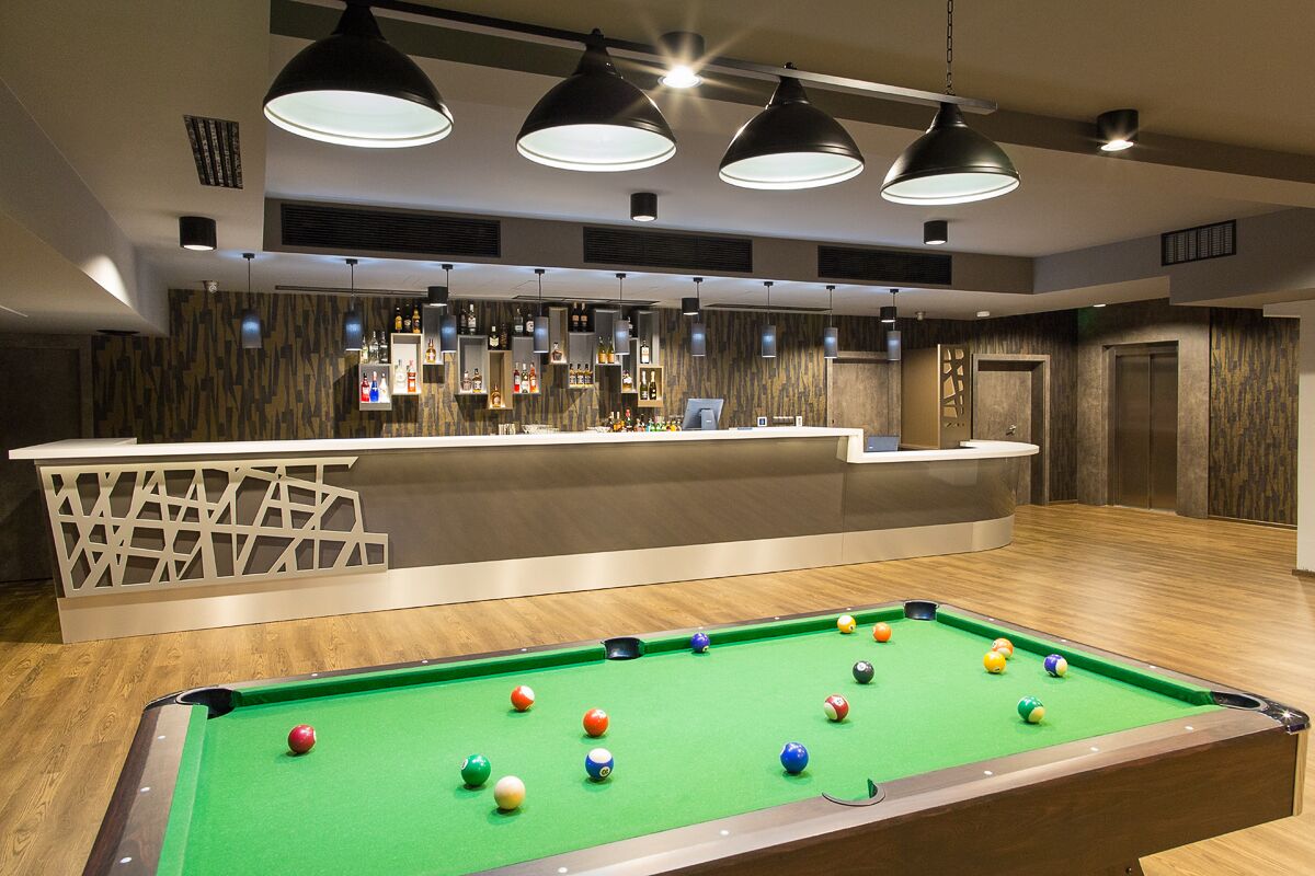 A pool table with balls, a bar area with bottles, and pendant lighting.